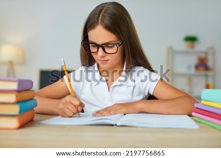Child at school. Kid writing in a notebook. Child doing homework. Serious focused student girl in glasses writing an essay at her desk in the classroom. Back to school, education, learning concept Royalty-Free Stock Photo #2197756865