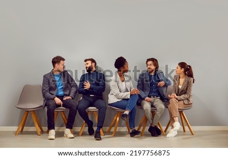 Young diverse Multiracial people candidates for office worker job or managers talking to each other discussing upcoming job interview or company, sits in row next to wall. Labor market concept Royalty-Free Stock Photo #2197756875