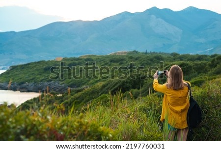 Woman with backpack photographs the mountains at sunset.