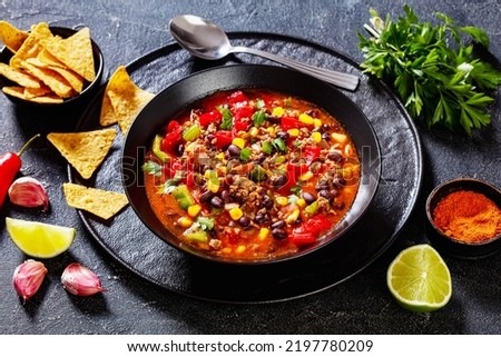 taco soup of ground beef, tomatoes, chopped green chilis, onions, corn, red beans and taco seasoning in black bowl,  landscape view