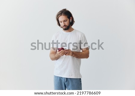 A man is holding a phone with wireless headphones in his ears and reading a social media message online freelancer job correspondence on a white background
