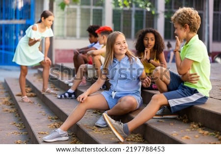 Children talking together while sitting on stairs outdoors. Youngsters chatting during summer day. Royalty-Free Stock Photo #2197788453