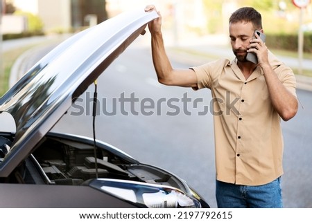 Sad driver calling car service, opening hood, having engine problem standing near broken car on the road. Car breakdown concept Royalty-Free Stock Photo #2197792615