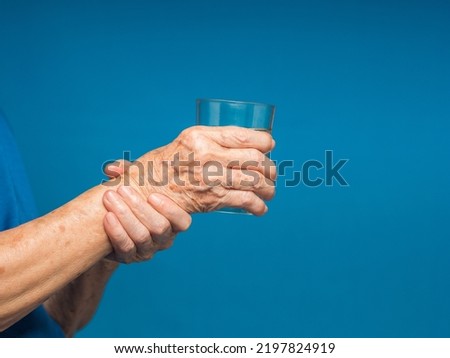Close-up of hands senior woman trying to hold a glass of water. Causes of hand shaking include Parkinson's disease, stroke, or brain injury. Mental health neurological disorder Royalty-Free Stock Photo #2197824919