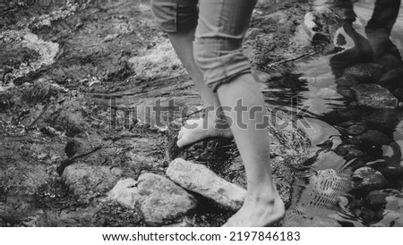 Girls with bare feet on the stones crosses a cold mountain stream. Black and white photograph.
