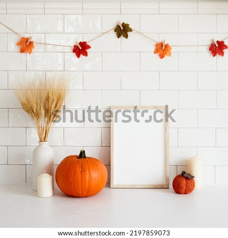 Autumn still life. Picture frame mockup, vase of wheat, orange pumpkins in cozy home room interior. Thanksgiving, Halloween, fall concept.