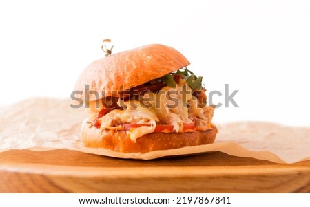 Burger with chicken fillet, pineapple, arugula, tomatoes, bacon and sauce on a wooden plate on a white background. Horizontal photo