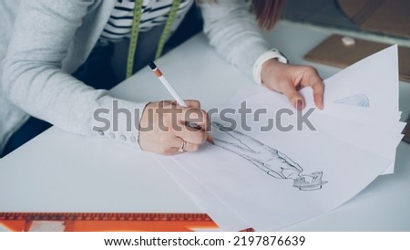 Close-up of fashion designer is drawing lines on clothing sketch. Woman is busy and concentrated on work.