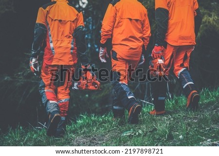 Men walking in the forest holding a chainsaw and garden tools. Lumberjacks at work wears orange personal protective equipment. Gardeners working outdoor in the forest. Security forestry worker concept Royalty-Free Stock Photo #2197898721