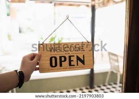 Hand woman hold open sign broad through the door glass. OPEN sign board through the glass of store window. text wooden board  door vintage shop sign opened store.