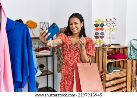 Young latin woman make selfie by the smartphone holding clothes at clothing store