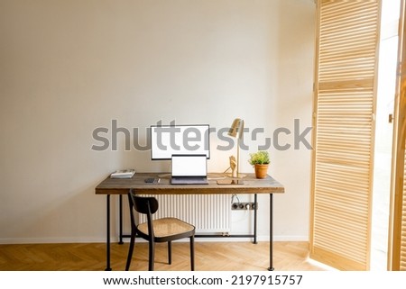 Workplace with computers on a wooden table in sunny room of stylish apartment. Mockup image with copy space on screens