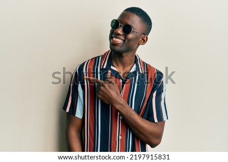 Young african american man wearing casual clothes and sunglasses smiling cheerful pointing with hand and finger up to the side  Royalty-Free Stock Photo #2197915831