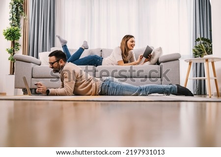 Smiling couple using technologies at home on their free time. Royalty-Free Stock Photo #2197931013