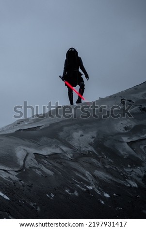 A fantastic assassin in a black suit with a red laser sword against a gray gloomy landscape of a snowy wasteland. dark photo with noise effect