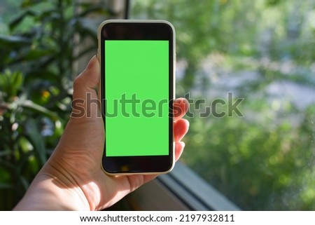 Women's hands hold a smartphone with an empty screen in nature. Chromakey. Place to copy