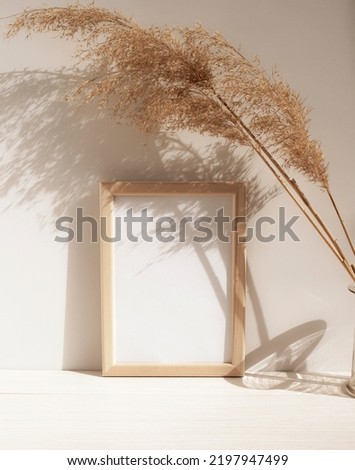 Empty white frame on the background of a white wall and dry branches in a glass flask. Template for design in natural colors. Side view. Vertical picture.