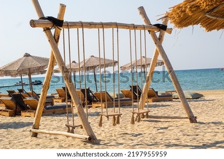Swing on a beach with sunbeds and parasols in background. Tropical sea picture with tropical swing. Near sea. visible sea. Rope swing