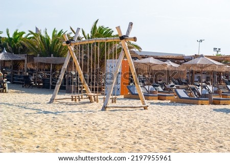 Swing on a beach with sunbeds and parasols in background. Tropical sea picture with tropical swing. Near sea. visible sea