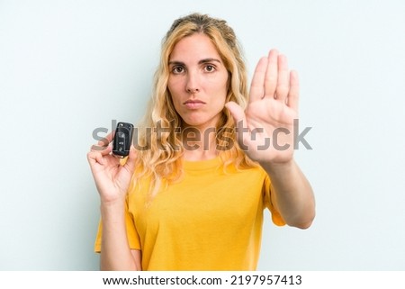 Young caucasian woman holding car keys isolated on blue background standing with outstretched hand showing stop sign, preventing you.