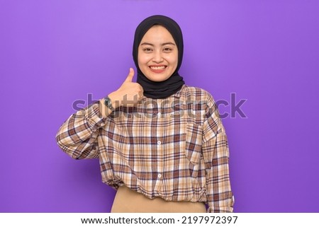 Cheerful young Asian woman in plaid shirt showing thumbs up isolated on purple background
