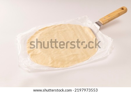 Pizza dough on baking paper on white background
