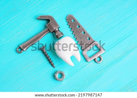 Human tooth model, steel hammer, wrench, handsaw, screw and nut isolated on a blue wooden background. Problems with dental equipment and materials concept.