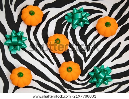 Kitschy Halloween or Thanksgiving composition with little pumpkins and green ribbons on zebra print background.