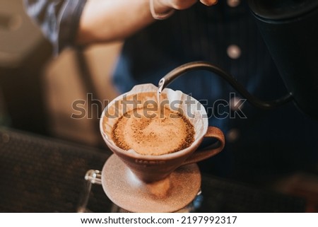 Professional barista making filtered drip coffee in coffee shop. Close up of hands barista brewing a drip hot espresso, pour over coffee with hot water and filter paper in cafe. Royalty-Free Stock Photo #2197992317