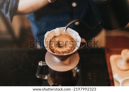 Professional barista making filtered drip coffee in coffee shop. Close up of hands barista brewing a drip hot espresso, pour over coffee with hot water and filter paper in cafe. Royalty-Free Stock Photo #2197992323