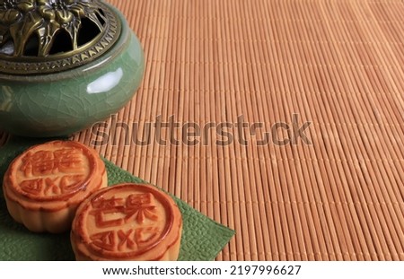 Chinese moon cake and incense burner on a bamboo background. Asian traditional mid-autumn festival. Translation of hieroglyphs: mango, pomegranate and lotus.