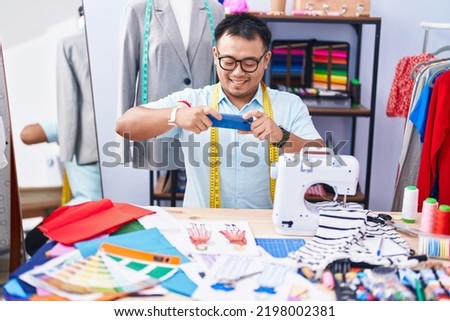 Young chinese man tailor make photo by smartphone to clothing design at tailor shop