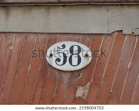 House number (address) fifty eight (58) sign, black numbered white plate (closeup) against red (orange) bricks wall of old building background. Grunge, texture, wallpaper