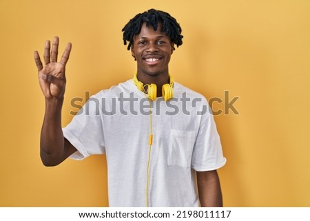 Young african man with dreadlocks standing over yellow background showing and pointing up with fingers number four while smiling confident and happy. 