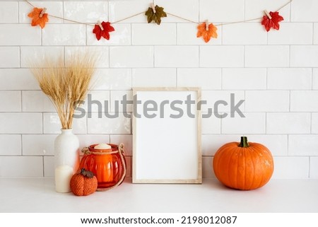 Picture frame mockup in cozy home interior with fall decor, vase of dried wheat, candle, pumpkin. Autumn, Thanksgiving, Halloween concept.