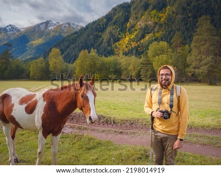 trip to Caucasus mountains, Arkhyz, Teberdinsky reserve. concept of discovery and exploration of wild places in early autumn. horse and hipster man in valley among autumn forest