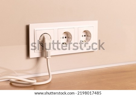 Group of white european electrical outlets with plug inserted into it on modern beige wall. Selective focus Royalty-Free Stock Photo #2198017485