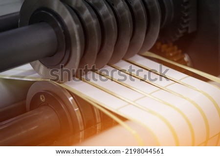 Rotating knives for cutting a self-adhesive label into several narrow ribbons. Equipment for the production of self-adhesive labels. Rotary die cutting machine with slitting blade. Selective focus Royalty-Free Stock Photo #2198044561