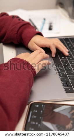 Child little boy working on laptop computer for learning and homework. Unfocused left hand with blurred foreground and background.