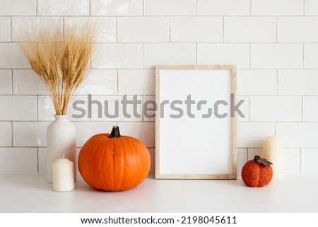 Cozy home interior with frame mockup, autumn fall decorations, pumpkins, vase of wheat, candle. Scandi, minimal style. Poster design for Halloween or Thanksgiving.