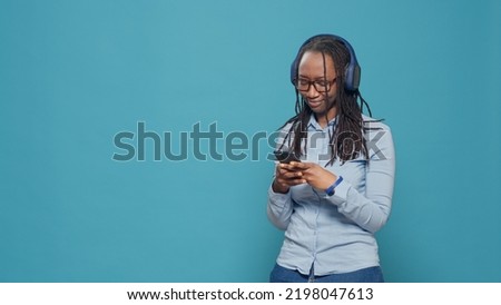 Female model using smartphone to listen to music on headset, having fun with radio song and dancing on camera. Looking at mobile phone and enjoying audio sound on earphones in studio.