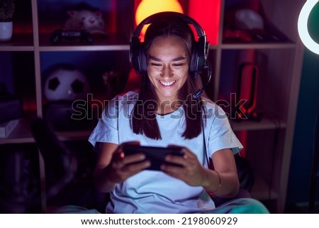 Young beautiful hispanic woman streamer playing video game using smartphone at gaming room