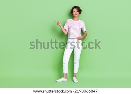 Full size photo of adorable young girl confident director point empty space wear stylish striped outfit isolated on green color background