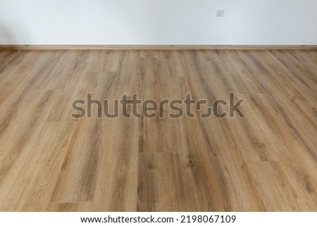 Laminated wood floor with white wall. Empty room with floating laminate in new apartmen Royalty-Free Stock Photo #2198067109