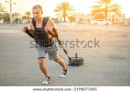 Handsome sporty man wearing a heavy jacket pulling weight sled outdoors.