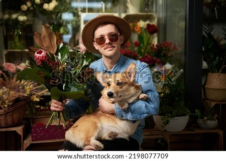 Hipster male person in sunglasses and hat with fresh spring flower bouquet and welsh corgi dog in flower shop. Mother's Day, Valentine's Day or International Women's Day concept. High quality image