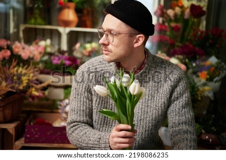 Bearded caucasian hipster male florist in sweater holding beautiful bouquet of spring white tulip bouquet. Valentine's Day, love, romantic or International Women's Day concept. High quality image