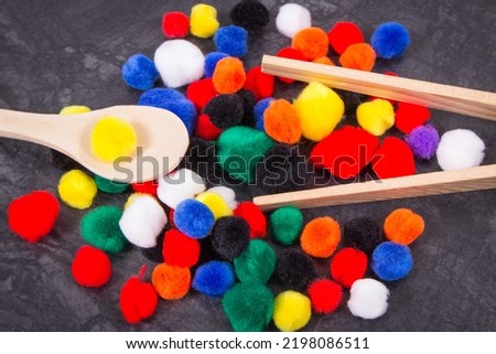 Small colorful pompoms with wooden spoon and tongs. Development of kids motor skills, coordination, creativity and logical thinking