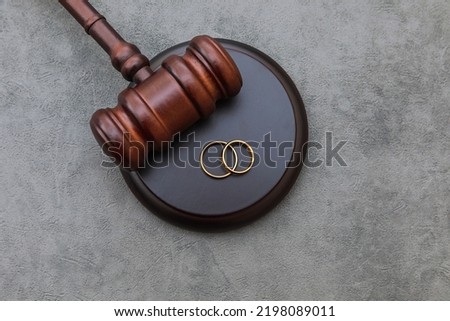 Law theme. Judge gavel wedding rings on concrete stone grey background. Divorce proceedings. Mallet of judge deciding on marriage divorce, marital agreement, legalities of divorce Royalty-Free Stock Photo #2198089011