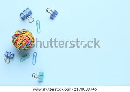 Colorful rubber band ball with paper clips on blue background